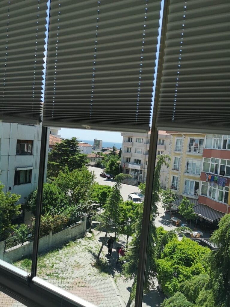 Jaluzi Cam balkon kanatlarında açık konumda gri plise perde